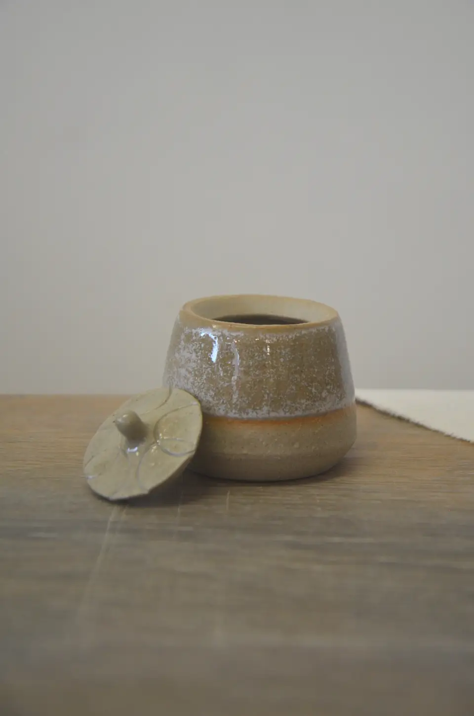 Pot beige moucheté, son couvercle posé à côté.
