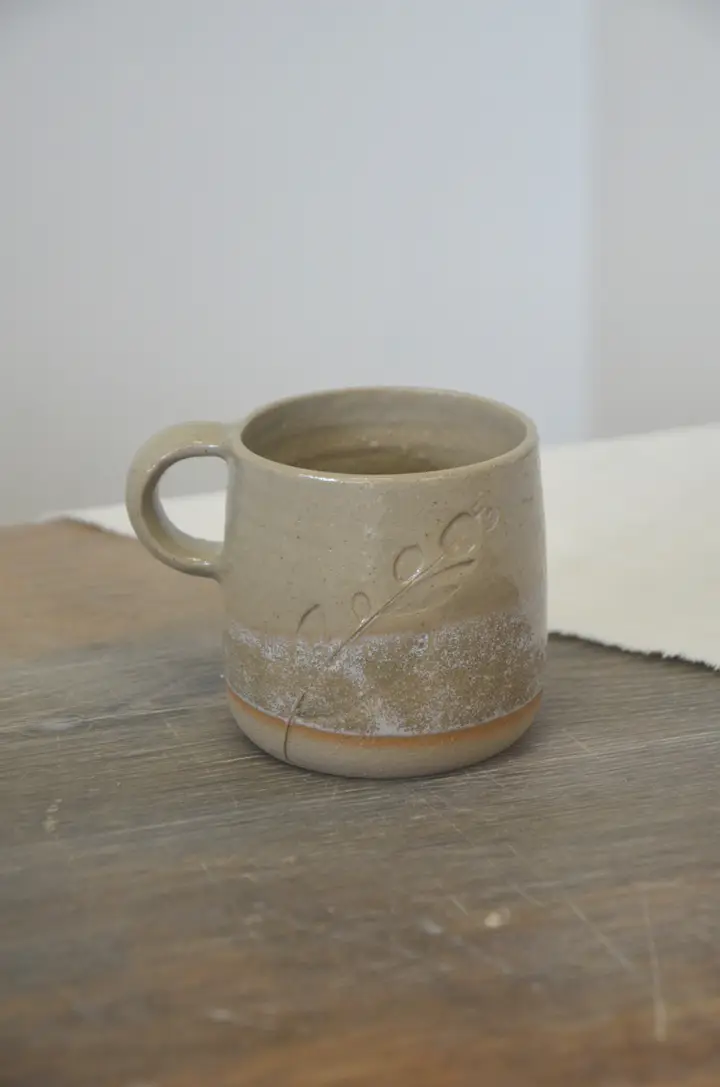 Tasse à anse beige et blanche, décor d'un brin végétal.
