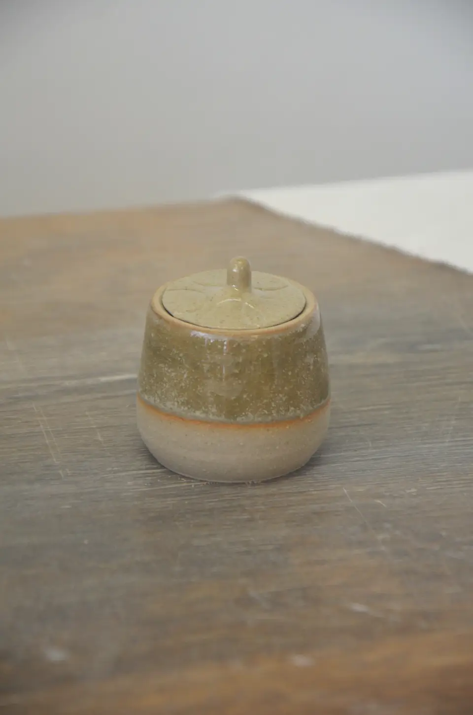 Petit pot à couvercle vert-brun sur une table en bois.