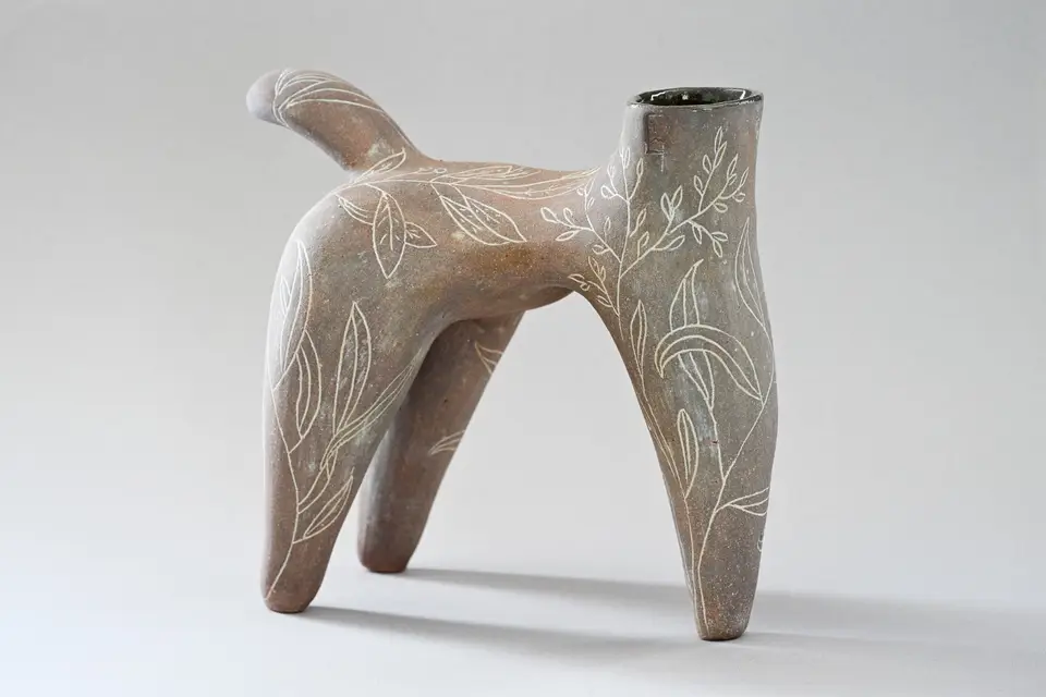 Pièce brune évoquant un animal à quatre pattes, ornée de feuillages blancs, sur fond gris.