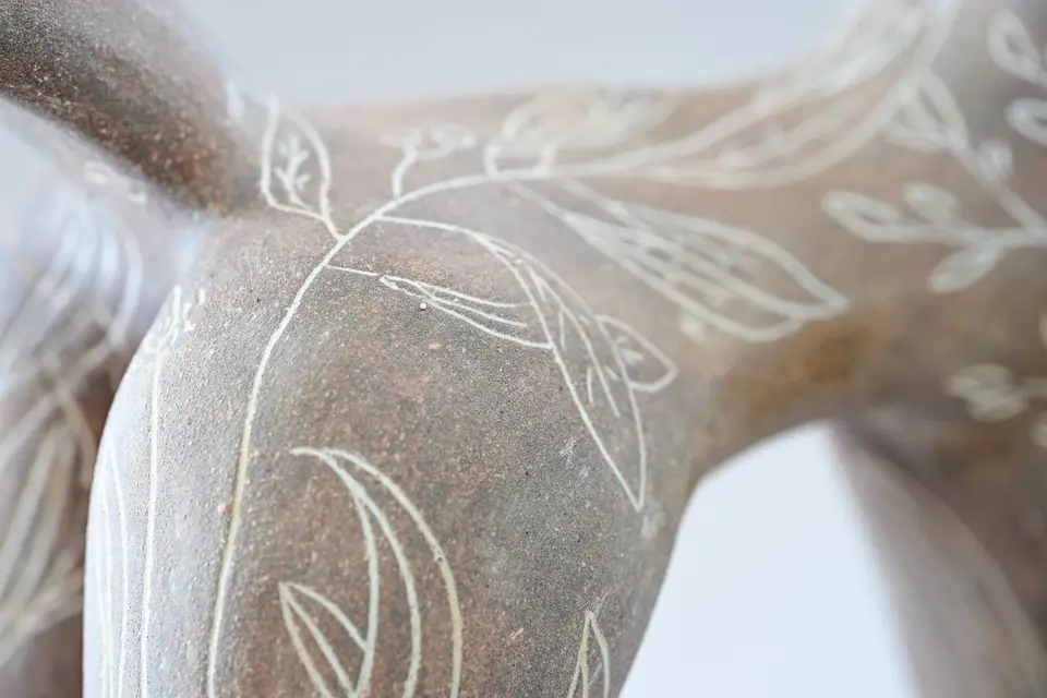 Détail d'une pièce brune couverte de feuillages blancs.